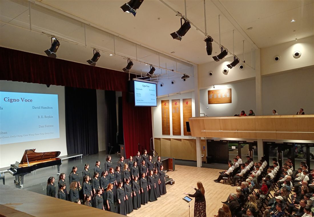 School choir performing on stage beside a grand piano