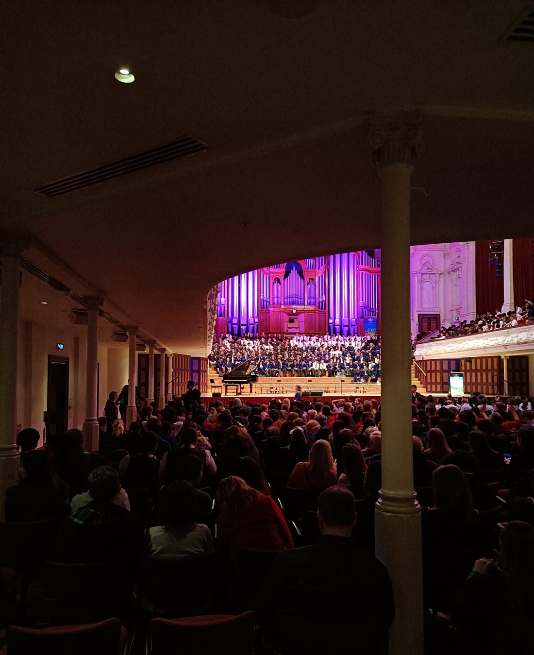 Concert hall stage lit in purple with a large pipe organ behind a massed choir